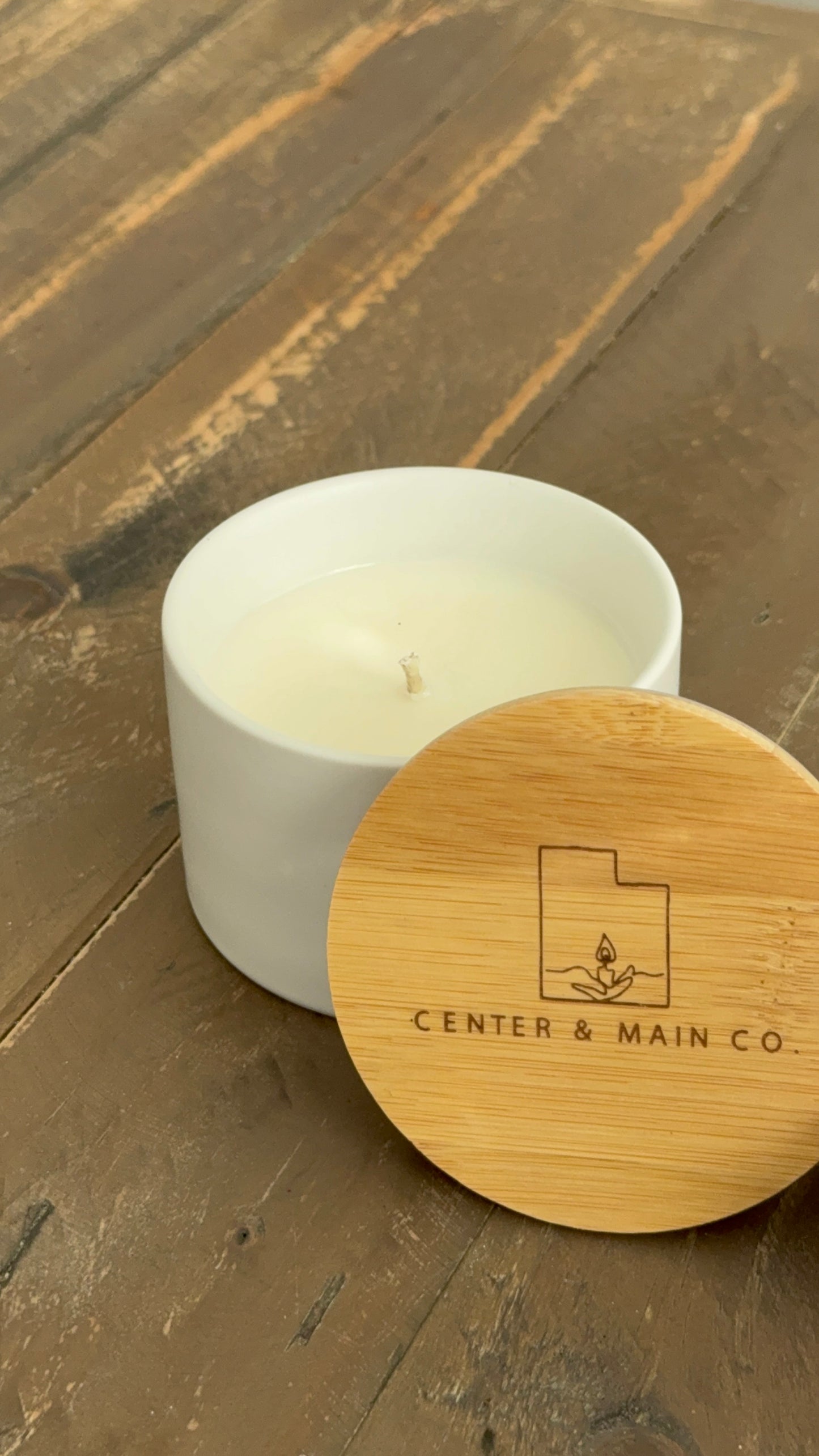side view of 5 ounce ceramic jar scented candle with lid on table. 