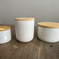 Three side view photos of white luxury candles with lids on a table. Scented candles on a table.